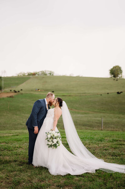 bride and groom kissing as they stand on a rug in the grass with a triangular wedding arch adorned with floral arrangements behind them at their Shenandoah wedding venue