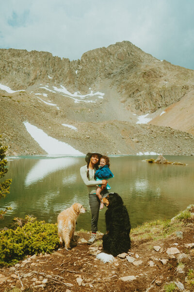 Colorado elopement photographer, Mikayla Renee Photo, on a hike with her daughter and two dogs in front of a high alpine lake