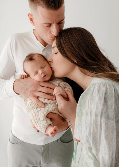 couple holding their brand new boy and kissing his cheeks in denver newborn photography studio