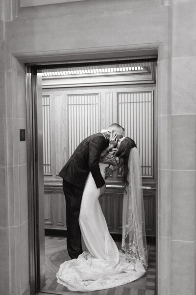 A newlywed couple sharing a romantic kiss in an elevator on their wedding day in San Francisco city hall