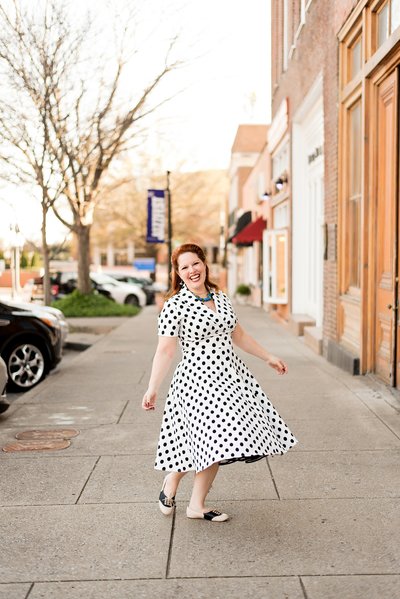 Raina from Weddings and Events by Raina wearing white and black polka dot dress spinning and laughing down on the Square in Murfreesboro