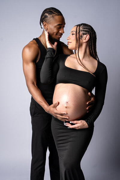 Pregnant couple embracing in studio lightting.