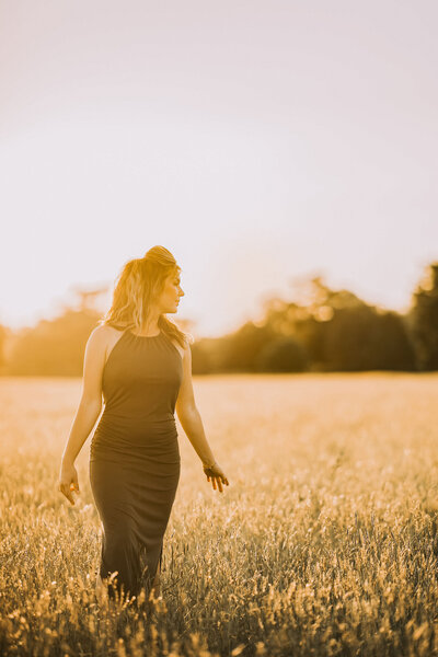 woman standing in a field in a green dress looking over her shoulder