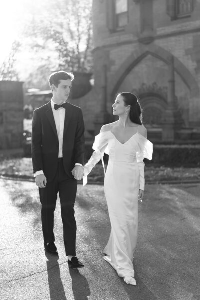 Black-and-white image of newlyweds walking hand-in-hand