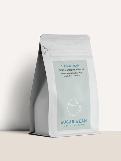 Branded Sugar Bean coffee bag for the ‘Handlebar’ roast featuring a soft mint label, sun and coffee cup icon, and tasting notes: caramel, chocolate, balanced.