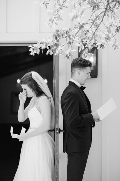 black and white photo of bride and groom with their backs to each other and reading their vows