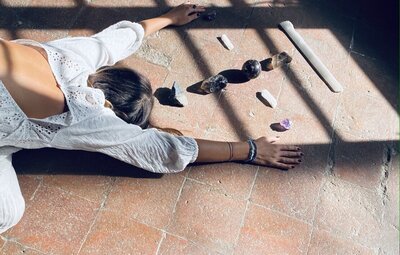 Leah Cavazzini practices Reiki and crystal healing, shown in a restorative pose surrounded by high-vibrational stones and natural sunlight, promoting deep energetic alignment and emotional release.
