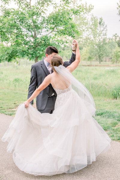 wedding portrait of groom twirling bride in a park