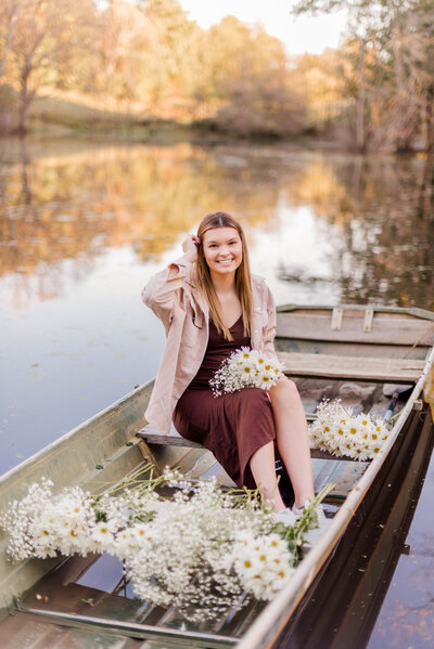 A teenage girl sits in a canoe on the lake with white flowers in her hand and scattering the canoe.