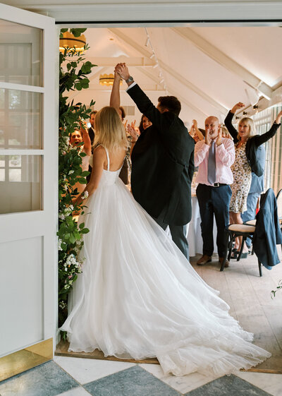 bride and groom entering room with arms raised