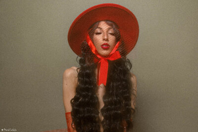 model wearing veiled red hat with long curly hair