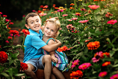 Little boy and girl hugging while sitting in a field of flowers.