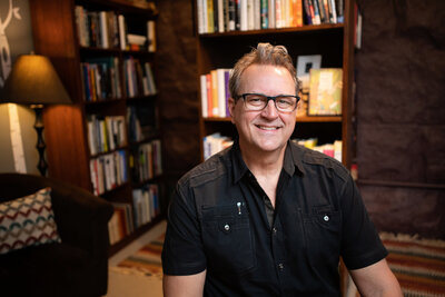 business headshot of author in front of bookshelves at Shelf Life bookstore in Cuyahoga Falls