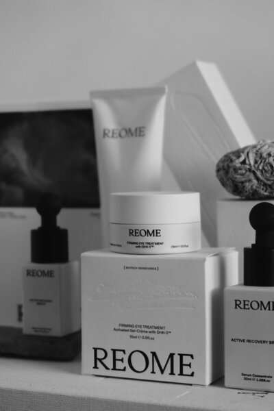 Black and white close-up of various Reome skincare products arranged in a neat, minimalist display, featuring a firming eye treatment and an active recovery serum.