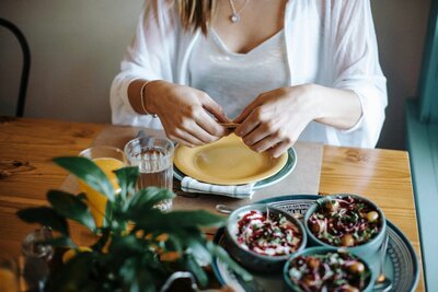 Woman setting a yellow plate at a table surrounded by fresh dishes and colorful vegetables, symbolizing mindful eating and home-cooked meals.