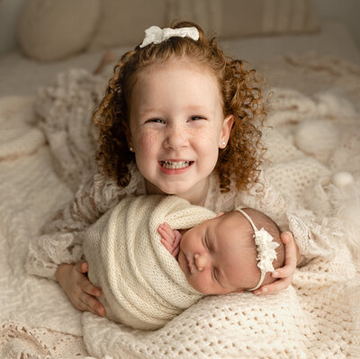 Big sister holding her infant sister looking so happy.
