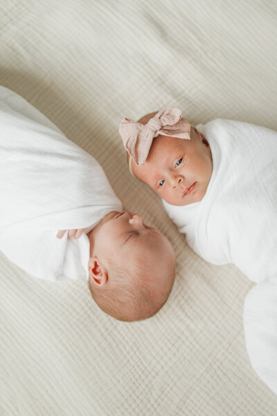 Twin babies lying on a blanket, one wearing a bow