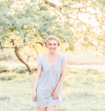 Bay area photographer, Amber Courtney, stands smiling in a field with glowing, golden hour light.