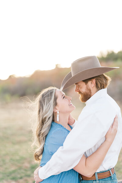 texas couple for engagement photos in a casual outfit with a cowboy hat and a blue dress, posing facing each other and smiling