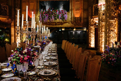 In the theater’s Grand Lobby, we designed a long, glowing dinner table that stretched through the golden interior. The table was layered with sequin linens, velvet napkins, tall candelabras, a whimsical shadowbox menu holder, and carved wooden chairs with black velvet seats.