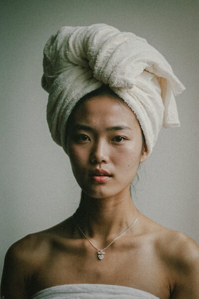 A member of "the women," with a towel wrapped around her head, dons a strapless garment and necklace against a plain background, embodying the elegance Sweet Pea Ink Creative is known for.