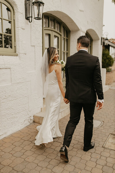 Wedding Photographer,  a bride and groom hold hands as they walk outside near old buildings