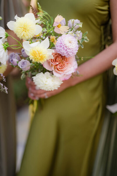 Bridesmaid holding a delicate, romantic bouquet with a textural mix of blooms in soft whites and warm pastels.