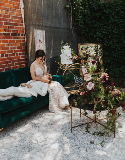 Brides on a couch, next to a cake, mirror, and calligraphy sign