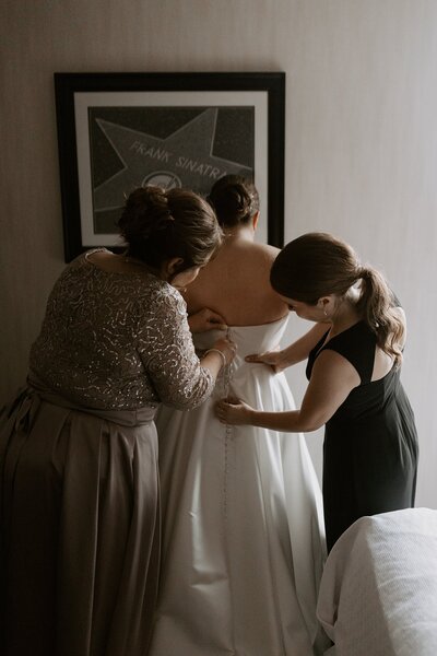 Mom and bridesmaid zipping bride into dress