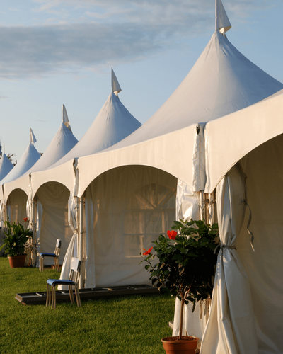 a row of large white tents with pointed tops are arranged on healthy green grass in preparation for an event