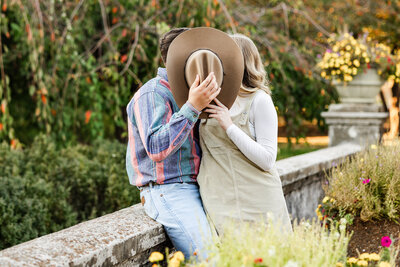 Couple kissing behind cowboy had leaning on a bridge