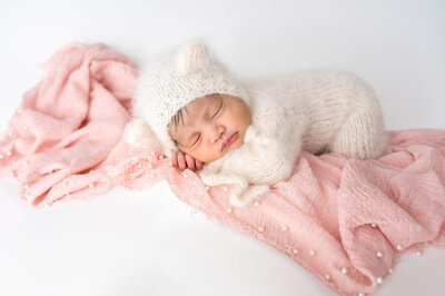 Baby dressed in a cream bear outfit is laying belly down in a pink pearl embellished fabric for a studio portrait in Chicago, IL