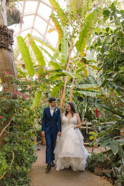 Bride and groom walking hand-in-hand inside a greenhouse filled with tropical plants at Denver Botanic Gardens
