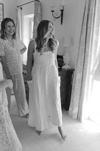 Bride getting ready on her wedding day as she looks at her fil-de-coupe scoop back wedding dress for the first time. The bride is wearing an embroidered linen coverup dress with scalloped details and pockets.