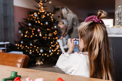 meisje maakt met haar roze fotocamera een foto van moeder en zoon bij de kerstboom