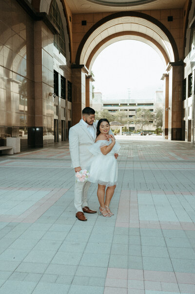 bride and groom pose under courthouse arch in downtown