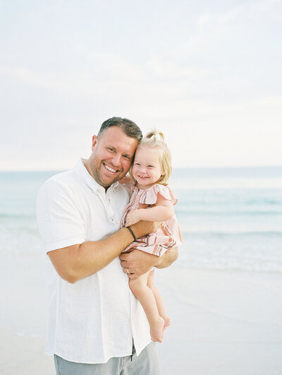 Dad holding his baby daughter and smiling in front of the ocean