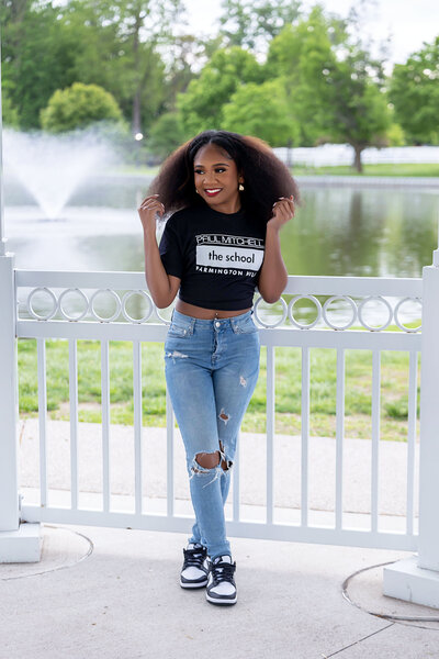 Senior girl wearing a black Paul Mitchell The School shirt and blue jeans leaning against a cabin wall
