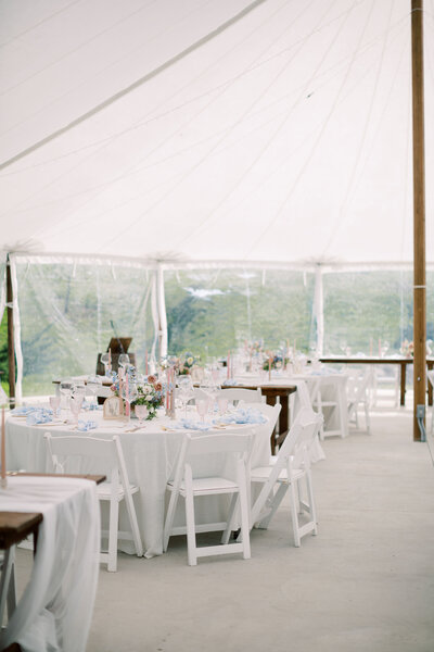 The interior of a white tented wedding venue with white chairs, tables with white cloths, and floral decorations 