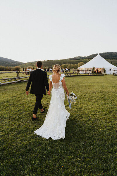 photo of bride and groom walking across a field towards wedding tent taken by Grand Teton elopement photographer