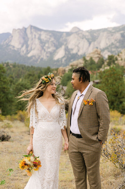 Joyful bride and groom holding hands at Knoll Willows in Estes Park on a windy day after their first look in the mountains.