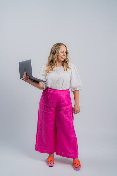 Amy Hart the Customer experience consultant holding a laptop and wearing pink pants