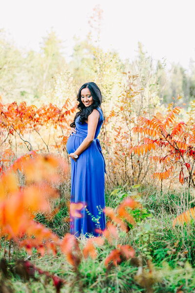 Excpecting mother in a blue maxi dress standing in an orange foliage