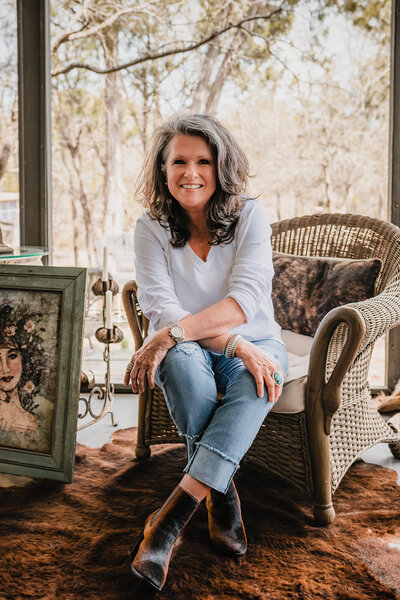 Home interior decorator and small business owner posing in her home sitting in a chair during branding session in Wimberley, TX.