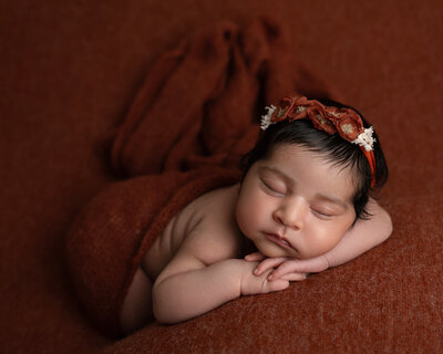 Newborn baby girl in a burnt orange wrap and floral headband during a studio session with Austin newborn photographer, Hello Photography