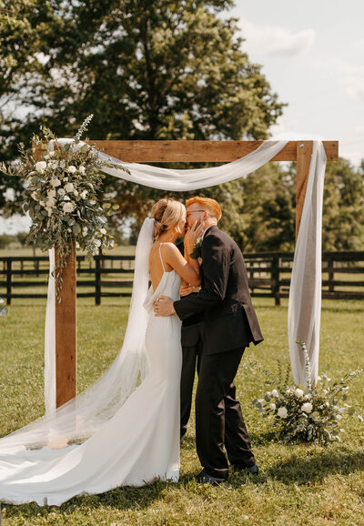 Kentucky bride and groom kissing under ceremony arch