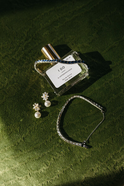 Bride flatlay of the bride's perfume, diamond bracelets, and pearl earrings on a green backdrop at the Farm at Old Edwards Inn in Highlands North Carolina, by Andrea-Marie Photography