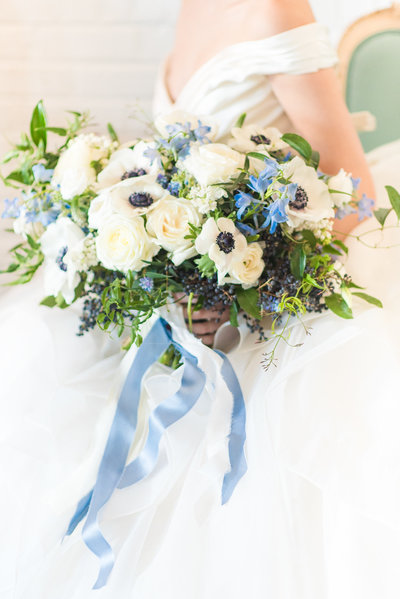 Elegant bride holding a blue and white bouquet with greenery