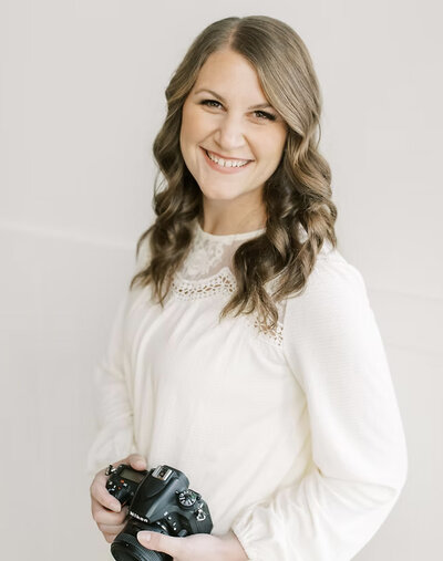 Megan smiling in a white blouse while holding a camera