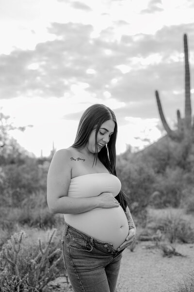 Black and white image of mother looking down at her belly against desert backdrop.